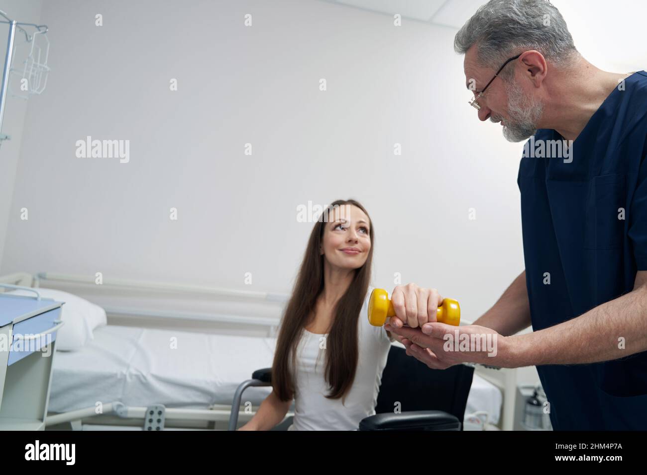 Woman with disability lifting one dumbbell supported by kinesiologist Stock Photo