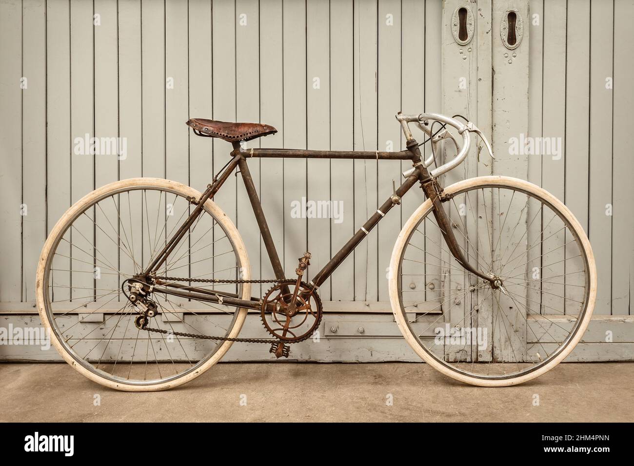 Vintage rusted racing bicycle parked in an old factory with wooden doors Stock Photo
