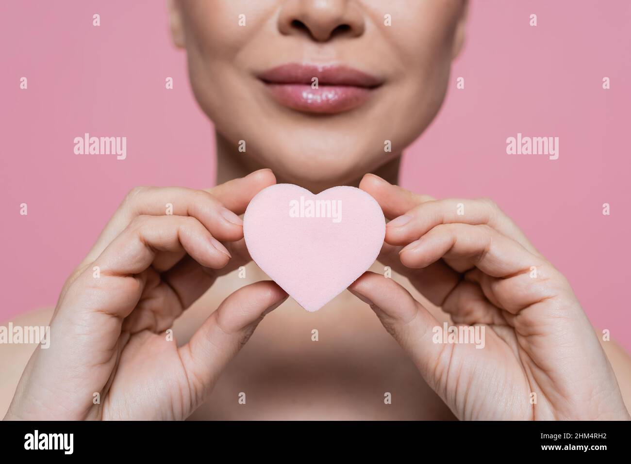 Cropped view of blurred woman holding heart shaped beauty blender isolated on pink Stock Photo