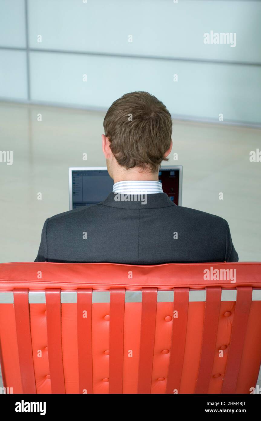Rear View Of A Businessman Sitting On A Chair And Using A Laptop, Credit:Photoshot Creative / Stuart Cox / Avalon Stock Photo