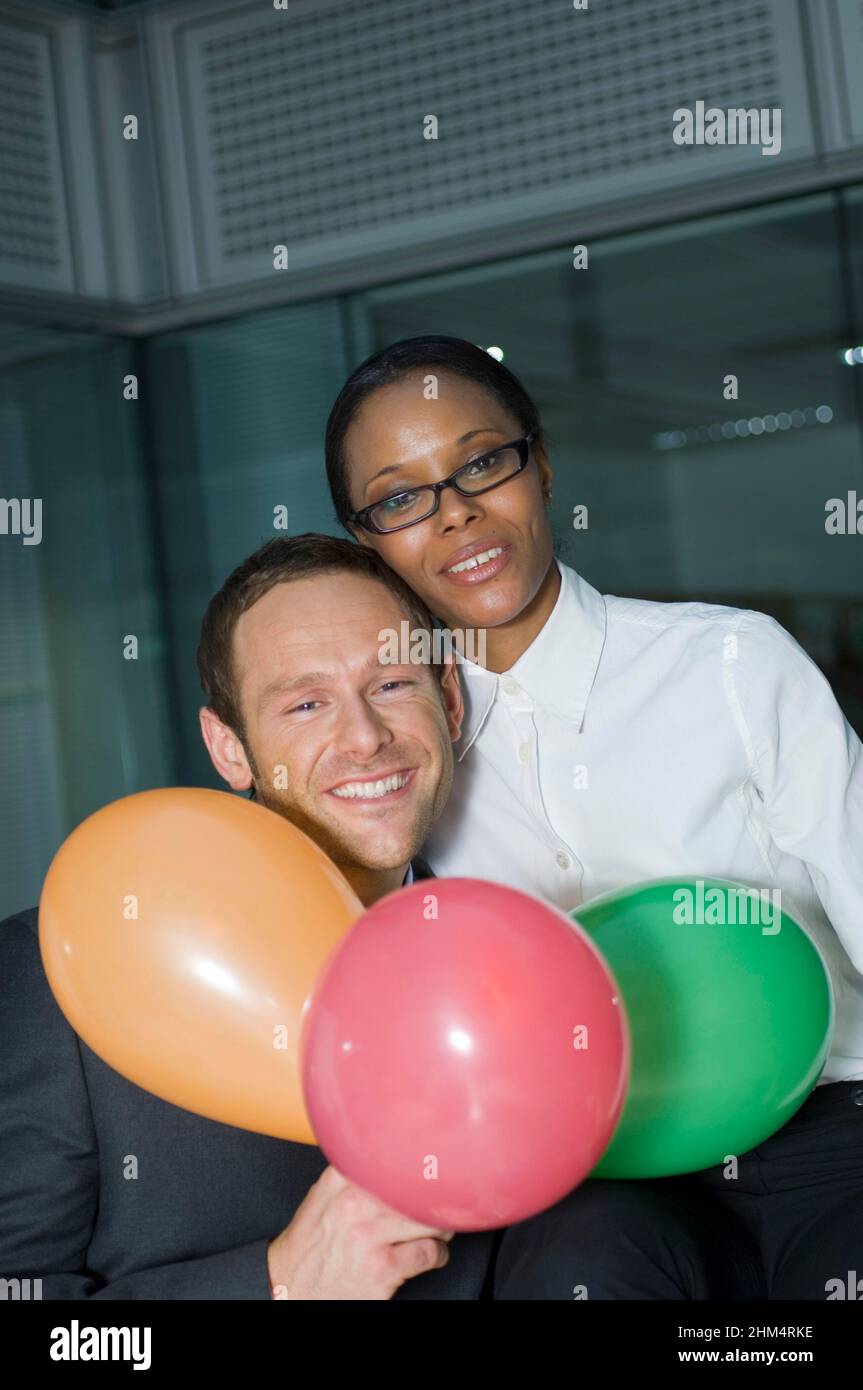 Portrait Of A Businessman With A Businesswoman Smiling And Holding Balloons, Credit:Photoshot Creative / Stuart Cox / Avalon Stock Photo
