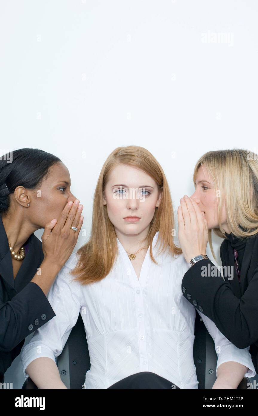 Portrait Of A Businesswoman Sitting On A Chair With Two Businesswomen On Either Side Whispering Into Her Ears, Credit:Photoshot Creative / Stuart Cox Stock Photo