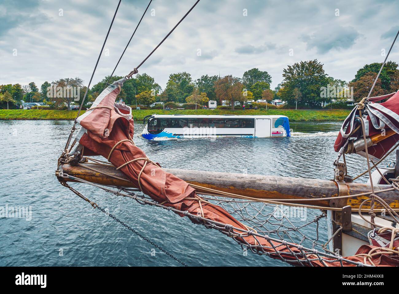 Ein Amphibienbus fährt auf der Trave an einem Segelschiff vorbei, das im Lübecker Museumshafen vertäut ist, im Hintergrund eine Gruppe von Wohnmobilen Stock Photo