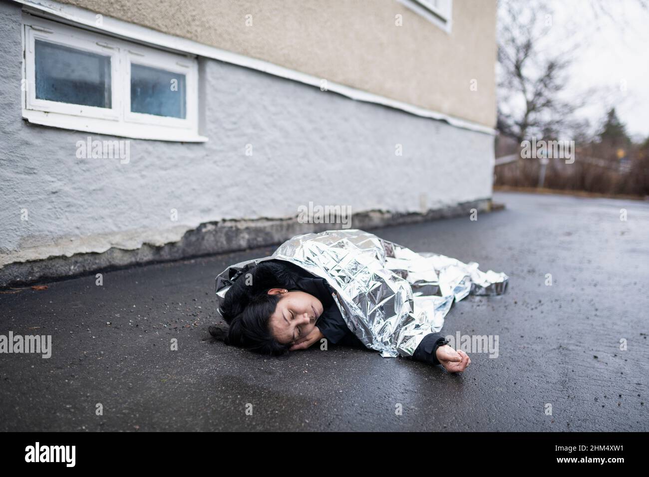 unconscious woman in medical shock lying under emergency blanket in street Stock Photo