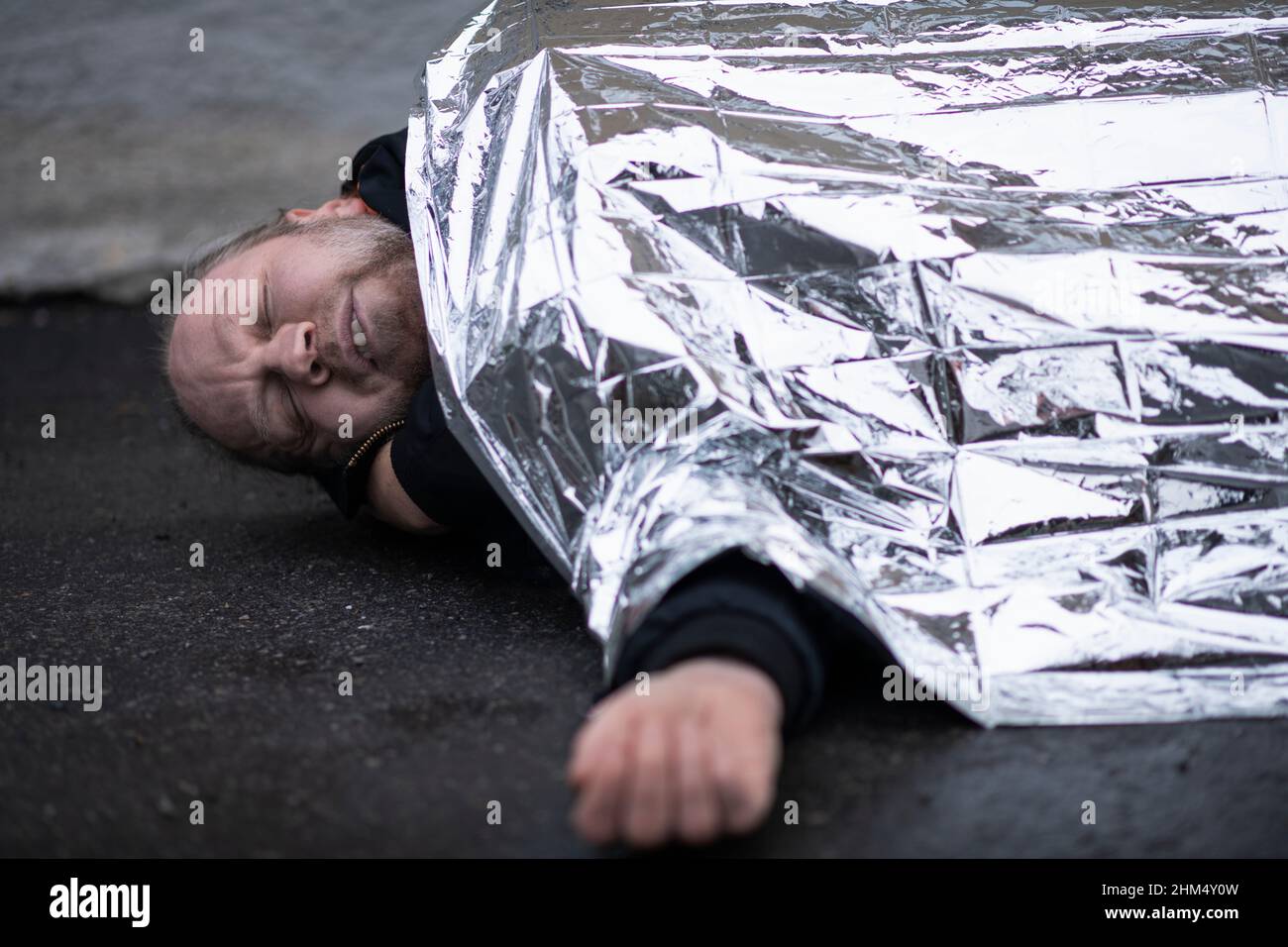 Unconscious man in medical shock lying under emergency blanket Stock Photo