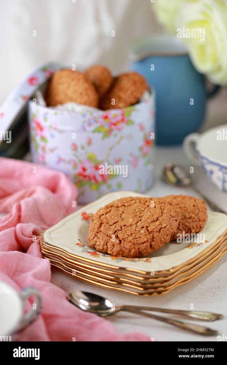 Table set with vintage crockery for traditional English afternoon tea with a biscuit tin and homemade biscuits on a plate Stock Photo