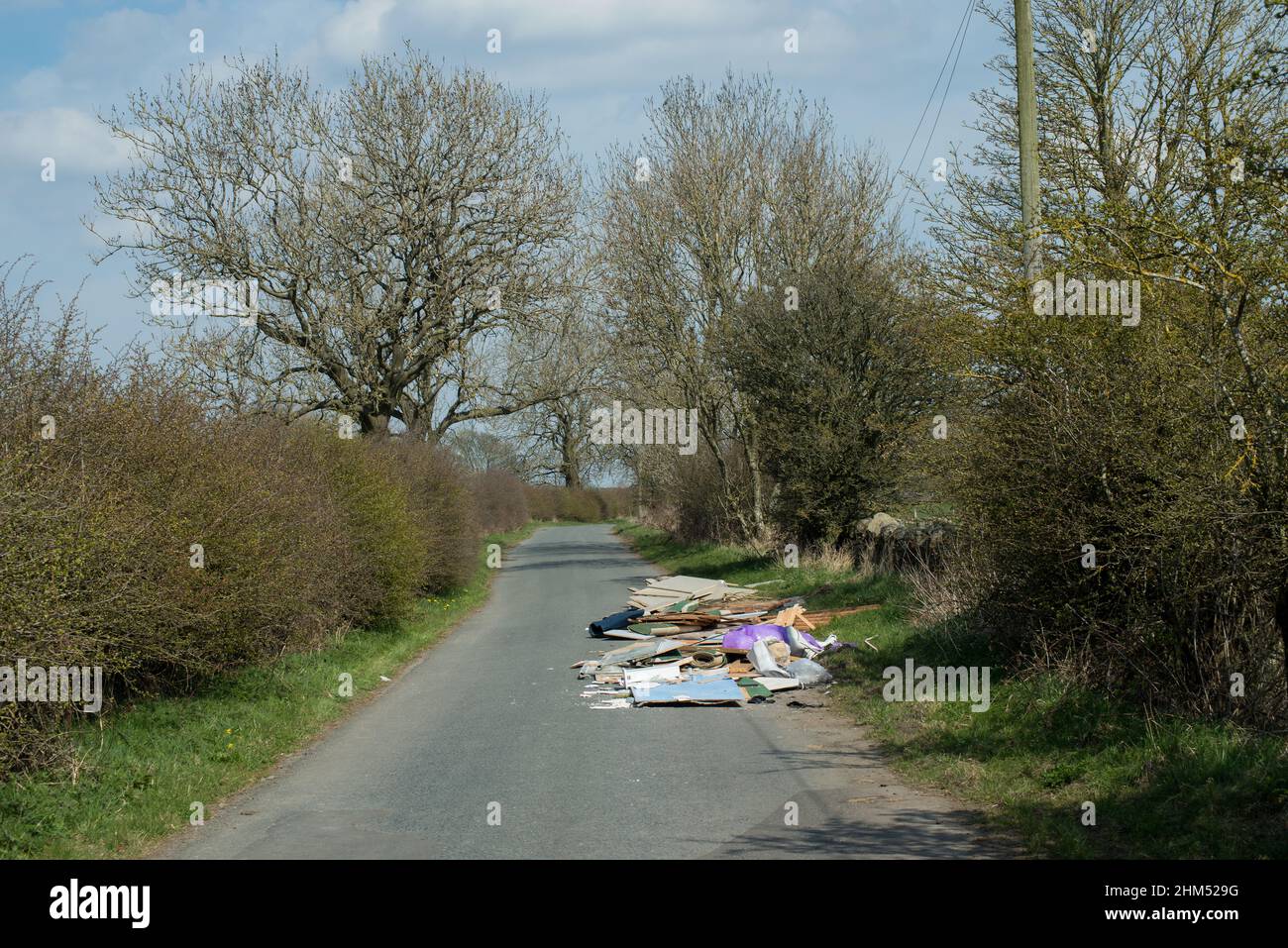 Fly tipping of household rubbish including glass and wood spreading across and almost blocking a narrow country road Stock Photo
