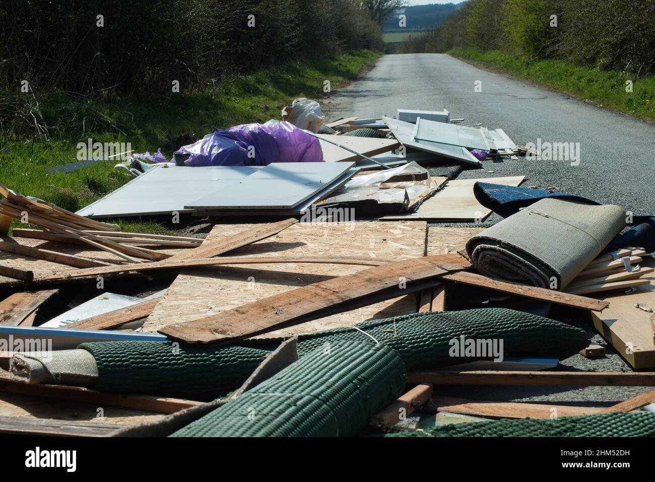 Close view of household clearance fly tipped onto and almost blocking a narrow country road causing a dangerous traffic problem. Stock Photo