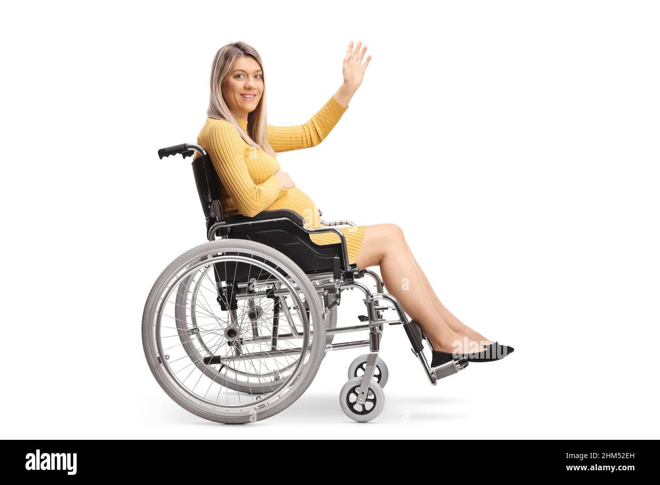 Full length profile shot of a pregnant woman sitting in a wheelchair and waving isolated on white background Stock Photo