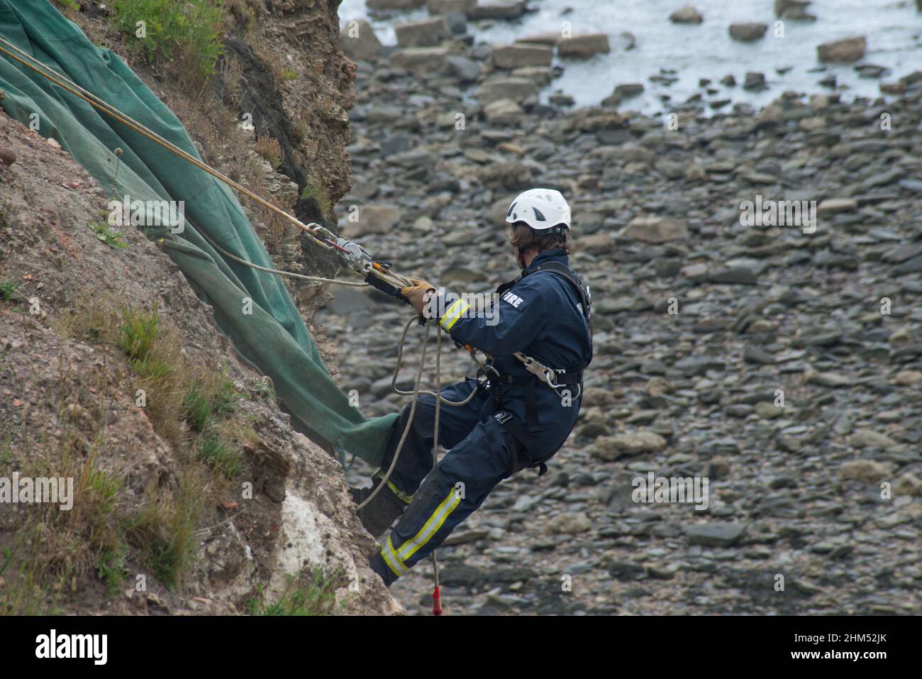 Member of fire crew in training about to descend coastal cliff face in mock rescue Stock Photo