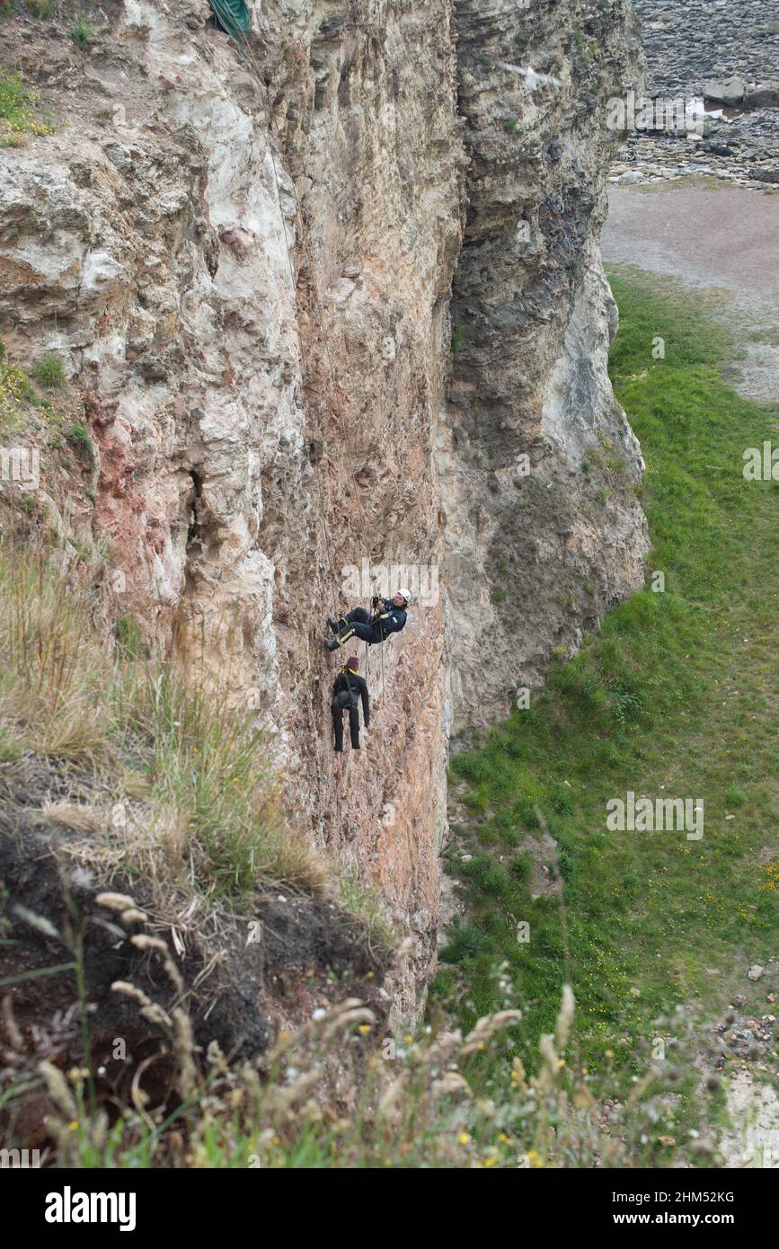 Member of fire crew approaches dummy on cliff face as part of a cliff rescue training exercise Stock Photo