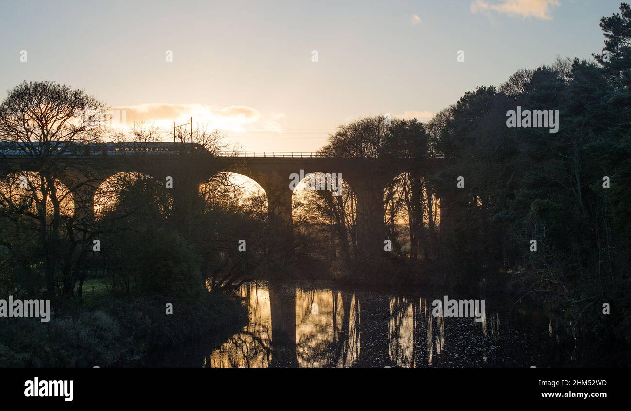 Train crossing viaduct spanning a river valley in the glow of an early winter sunset Stock Photo