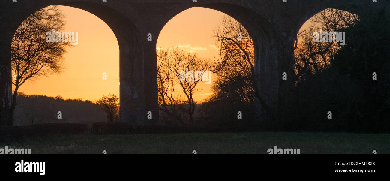Arches of a railway viaduct in silhouette with the golden light of a winters sunset behind Stock Photo