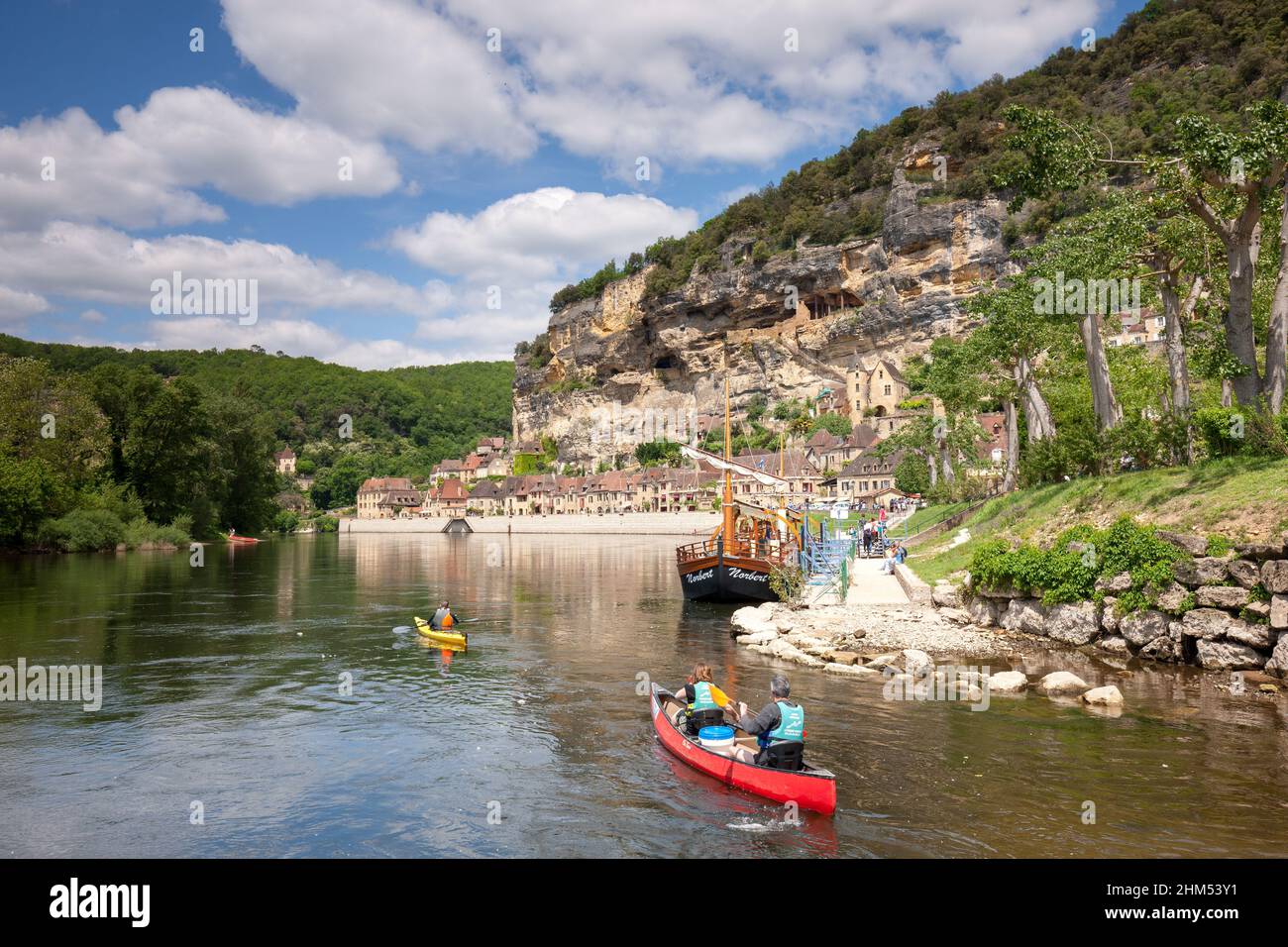 La Roque Gageac with pople canoeing ,cliffs and river boats in the summer sunshine and white clouds Dordogne France Stock Photo