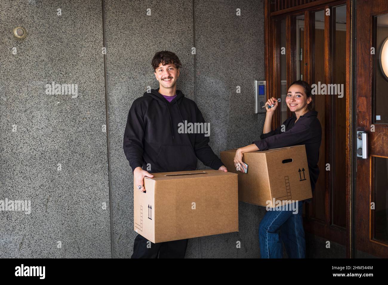 Smiling couple carrying boxes and holding keys Stock Photo