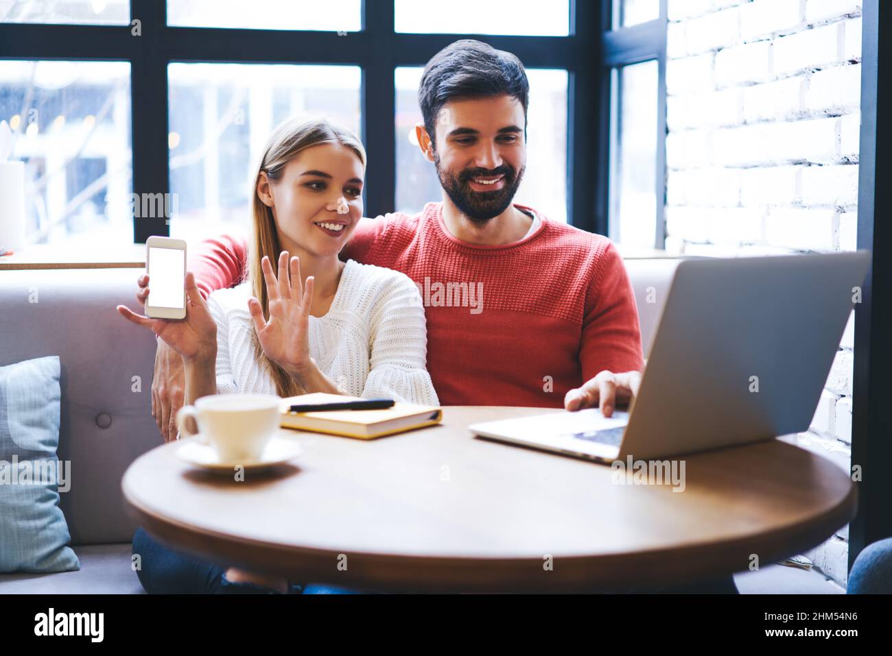 Smiling man and woman watching video on laptop in cozy cafeteria Stock Photo