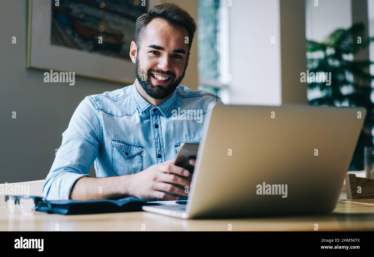 Smiling freelancer using smartphone while working on laptop Stock Photo