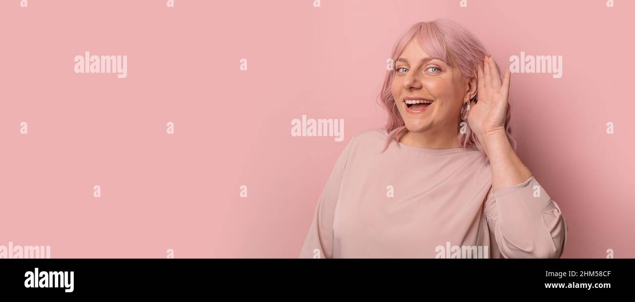 Shock, gossip, share advice. Young 30s woman smiling with hand over ear listening and hearing to rumor over pink background. Stock Photo
