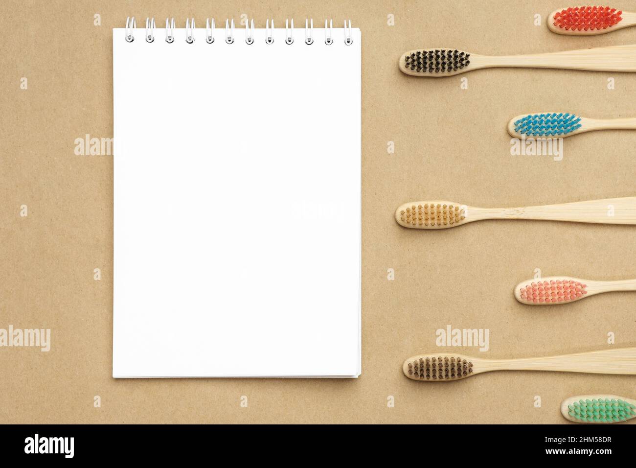 Multiple multicolor bamboo toothbrushes are lying on craft eco paper near notepad. Copy space, top view. Stock Photo