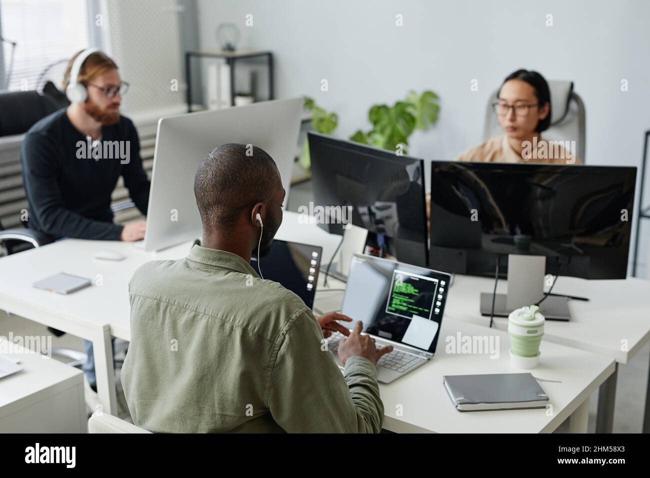 Three young intercultural diversity programmers sitting by desks in ...