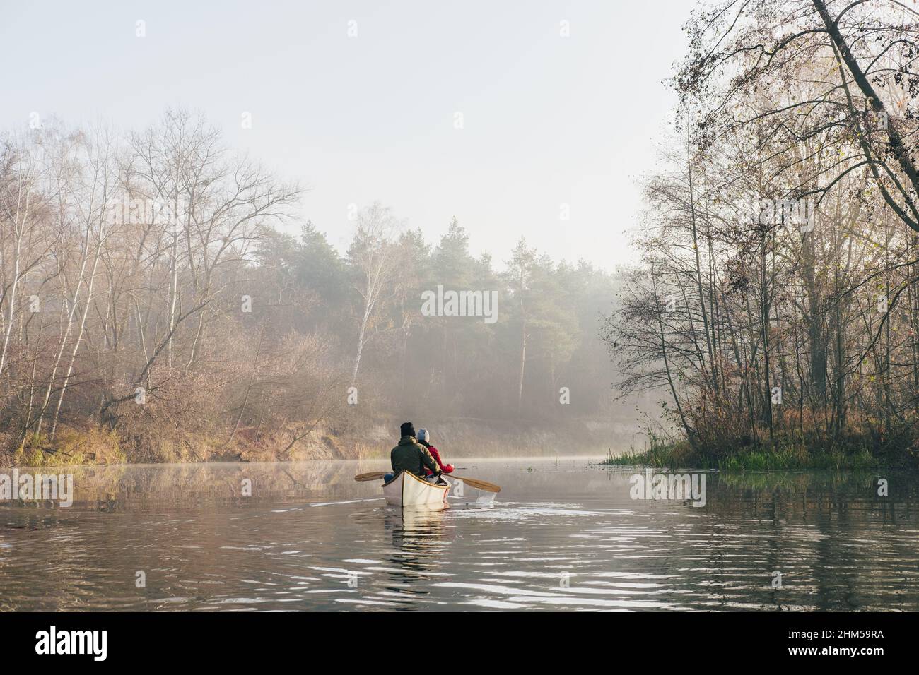Two people in a canoe paddling on a calm river, misty morning scene ...