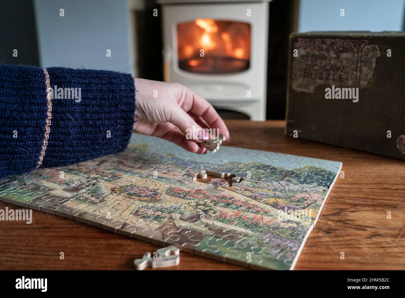 A woman sits next to a wood burning stove as she pieces together a vintage  Victory Artistic 1930s wooden puzzle Stock Photo - Alamy