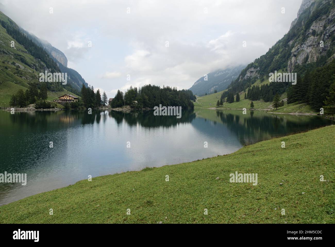berggasthaus seealpsee switzerland, big lake in total view, with island and restaurant hotel, cloudy summer day, mystical atmosphere Stock Photo