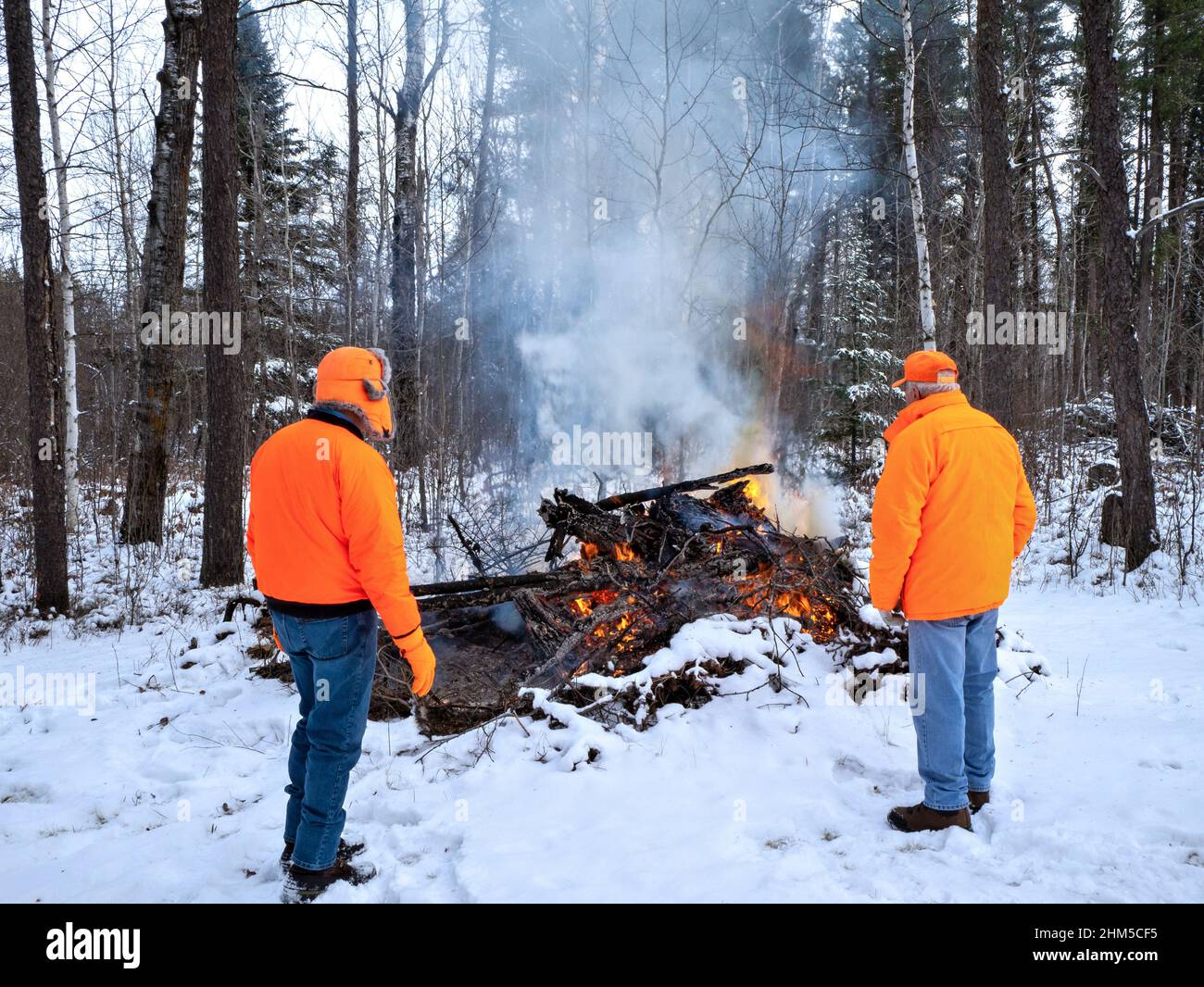 Two men wearing hunter orange watch a controlled brush fire Stock Photo