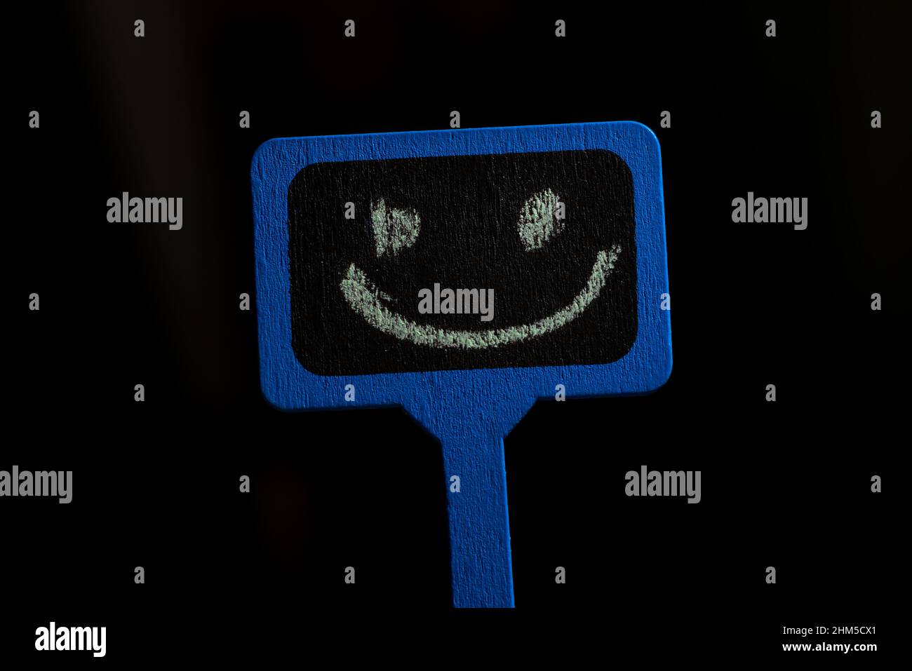 A sign with a smiley face. Blue wooden poster with a positive smile on a black background. Stock Photo