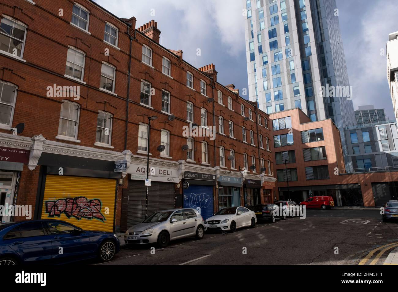 Old red brick buildings on Leyden Street are loomed over by one of the numerous towers in the City of London on 4th February 2022 in London, United Kingdom. The City of London is a city, ceremonial county and local government district that contains the primary central business district CBD of London. The City of London is widely referred to simply as the City is also colloquially known as the Square Mile. Over the last decade or so the architecture of the City has grown upwards with skyscrapers filling the now cluttered skyline, and increasing it’s scale upwards with glass towers, some of whic Stock Photo