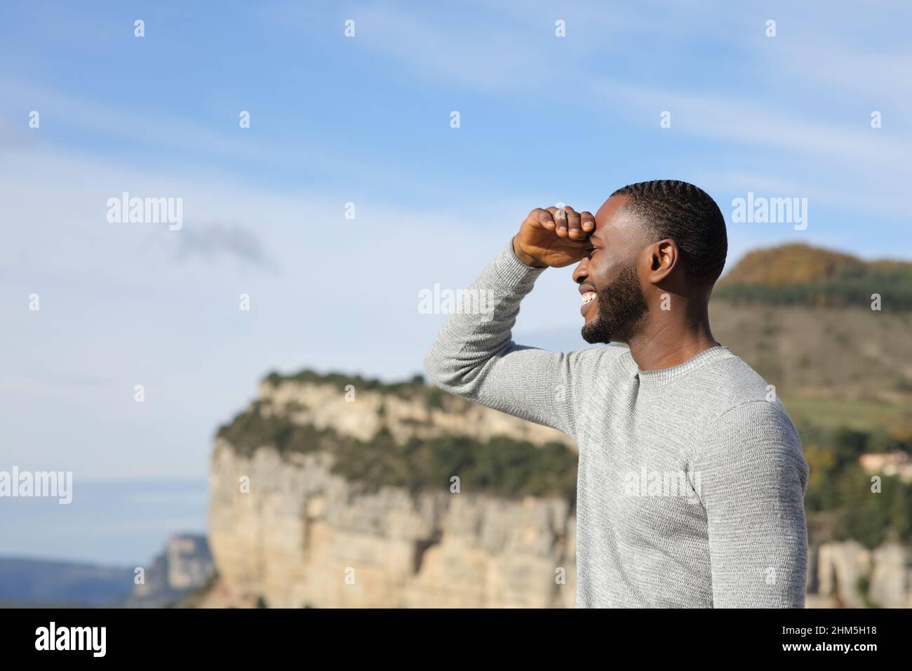Happy man with black skin searching looking away protecting from sun with his hand in the mountain Stock Photo