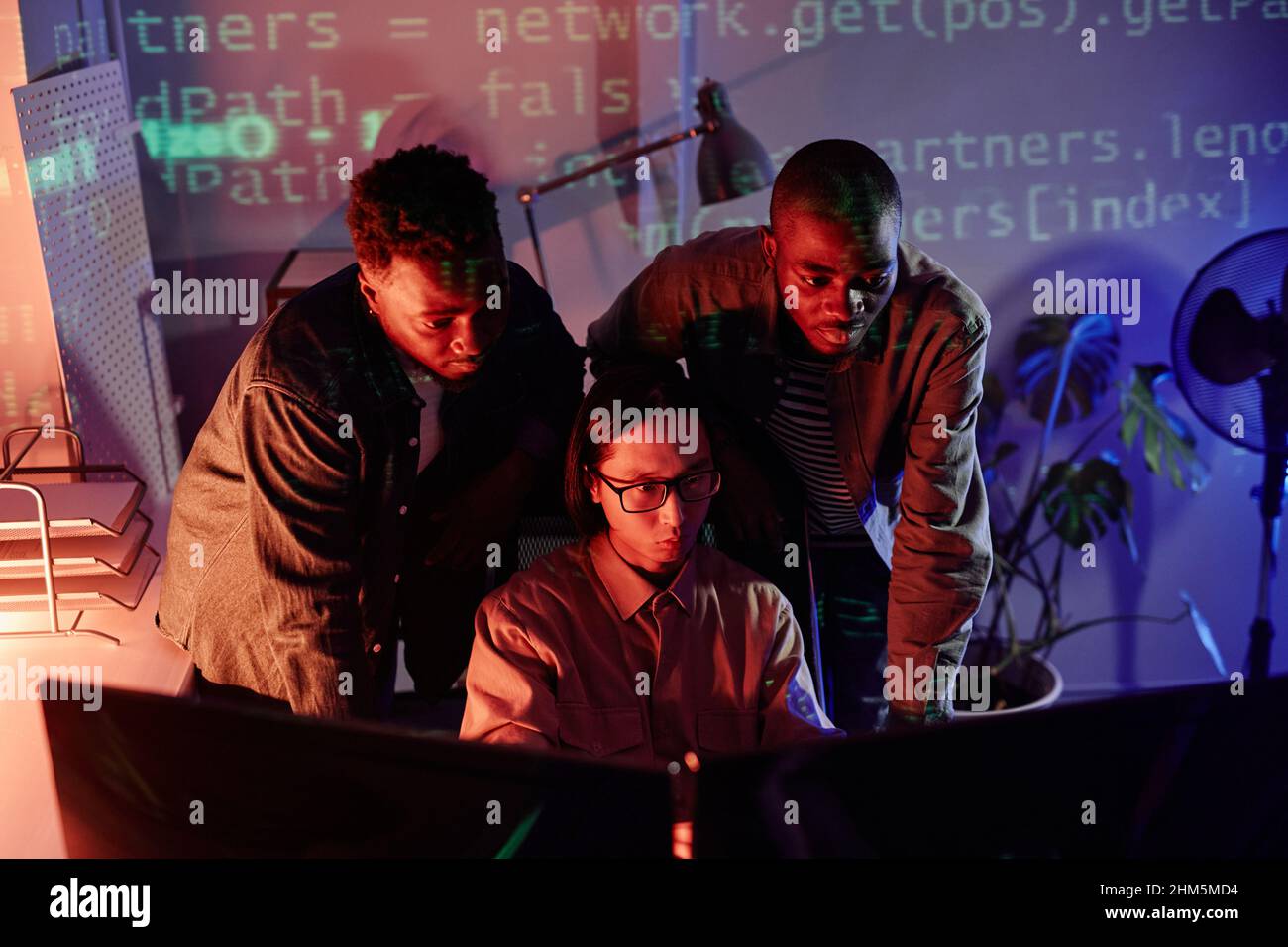 Group of young intercultural programmers bending in front of computer monitors while decoding data or developing new software Stock Photo