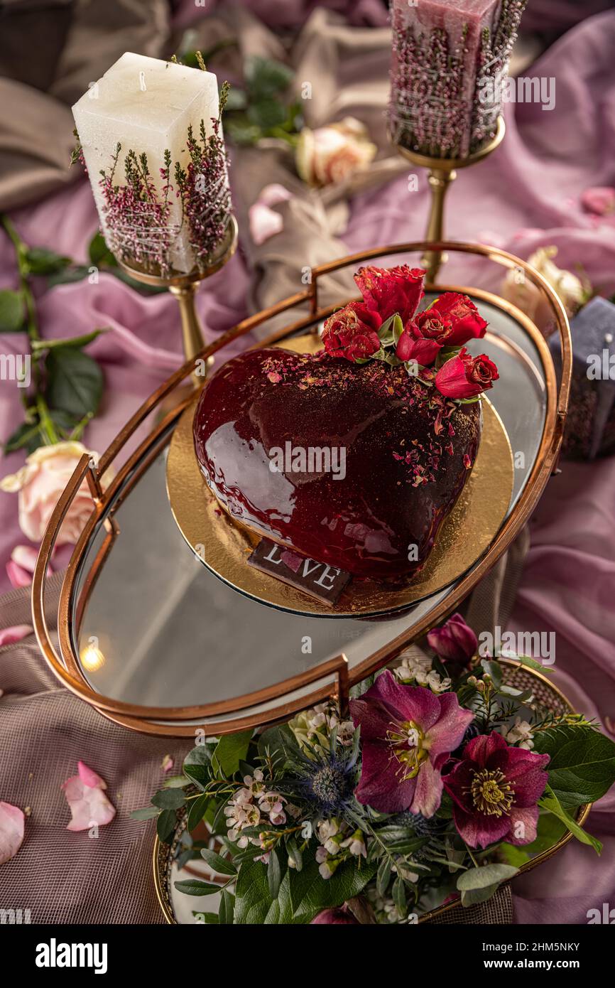 Valentine's day or wedding cake still life concept. Modern mousse cakes with red mirror glaze in the shape of a heart decorated with rosary Stock Photo