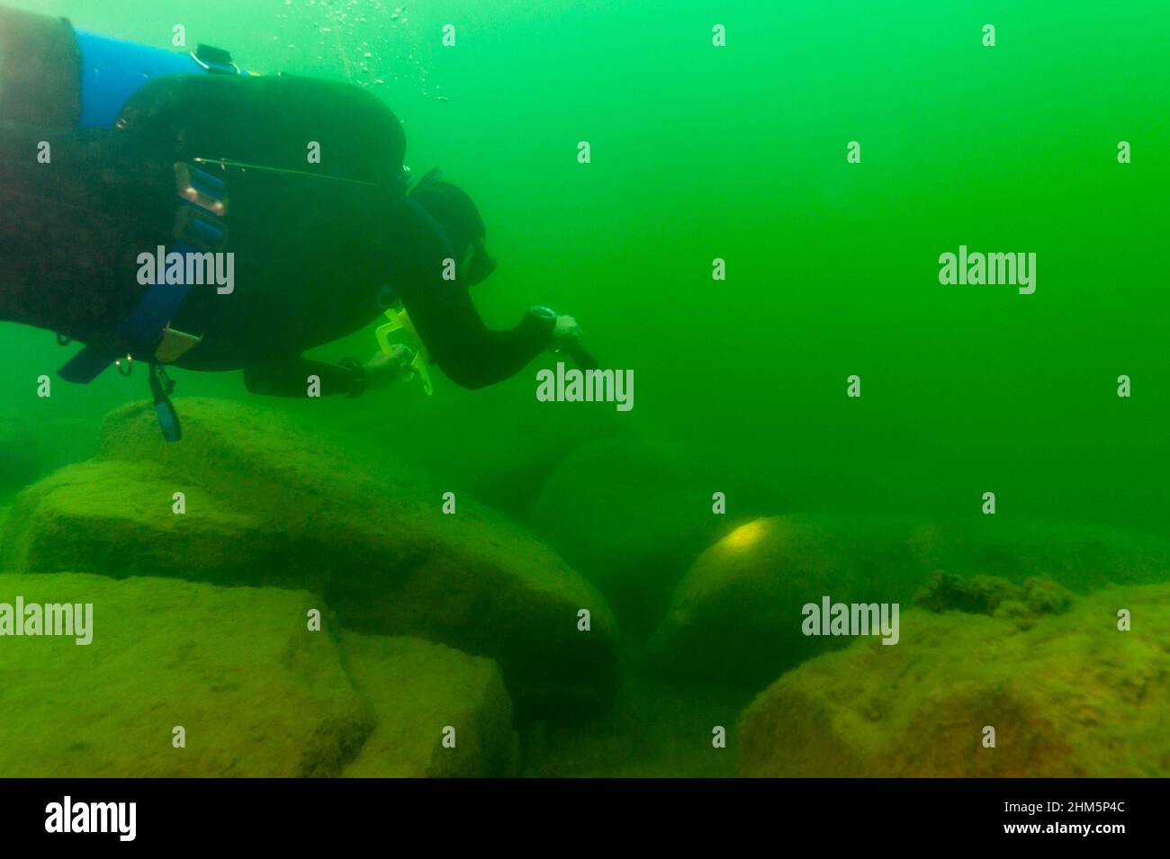SCUBA diver exploring a cloudy inland lake and boulders with a diving