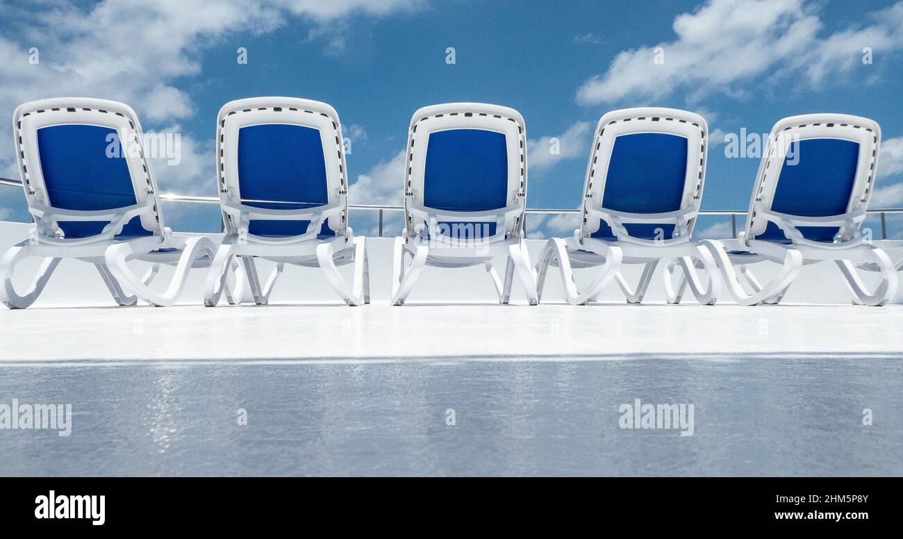 Five blue sun loungers in daytime with blue sky on the deck of a