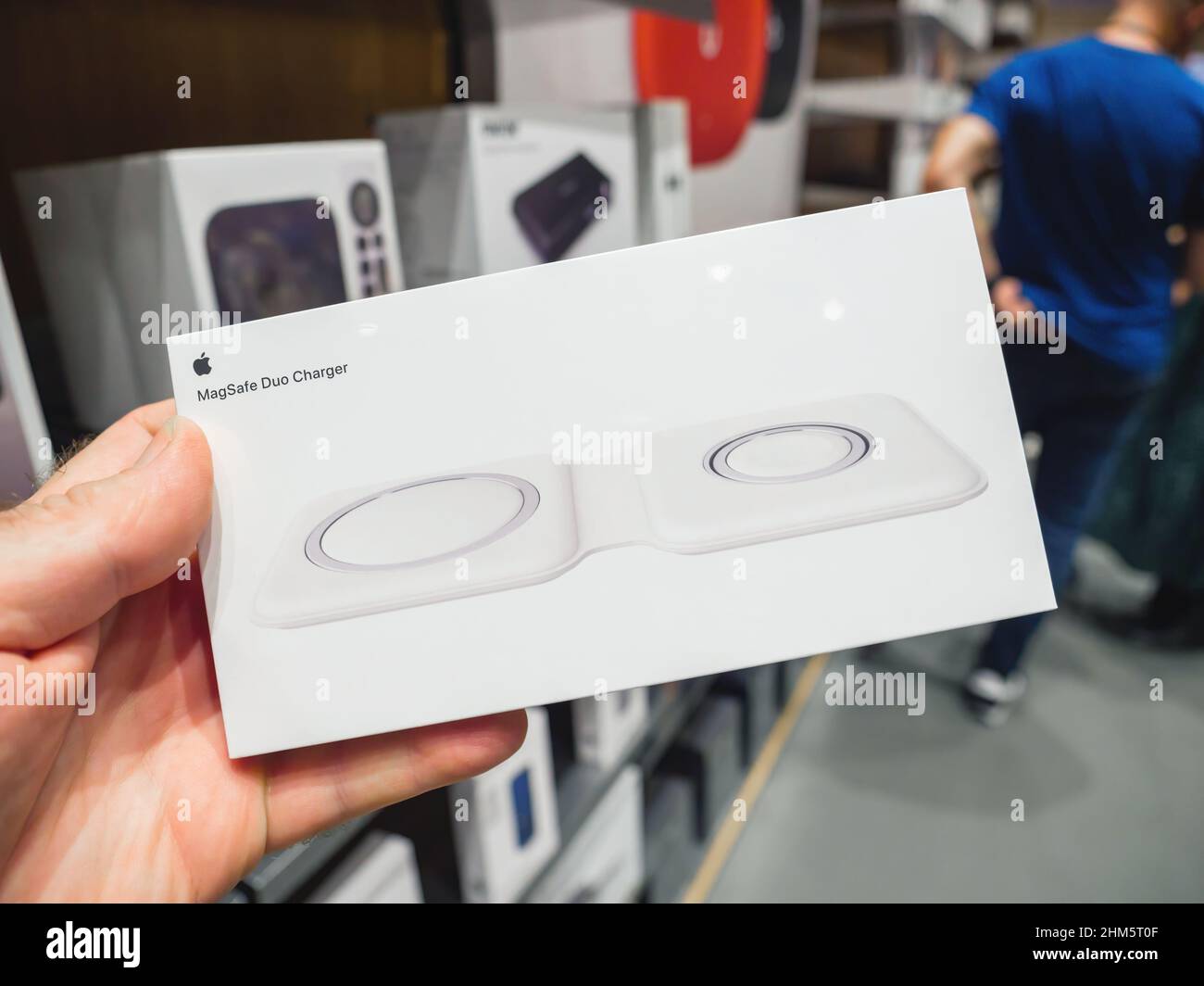 Paris, France - Sep 24, 2021: POV male hand holding new Apple Computers Mag Safe Duo Charger for iPhone and Apple Watch magnetic charger with customers defocused in background - accessory to charge wirelessly the iphone Stock Photo