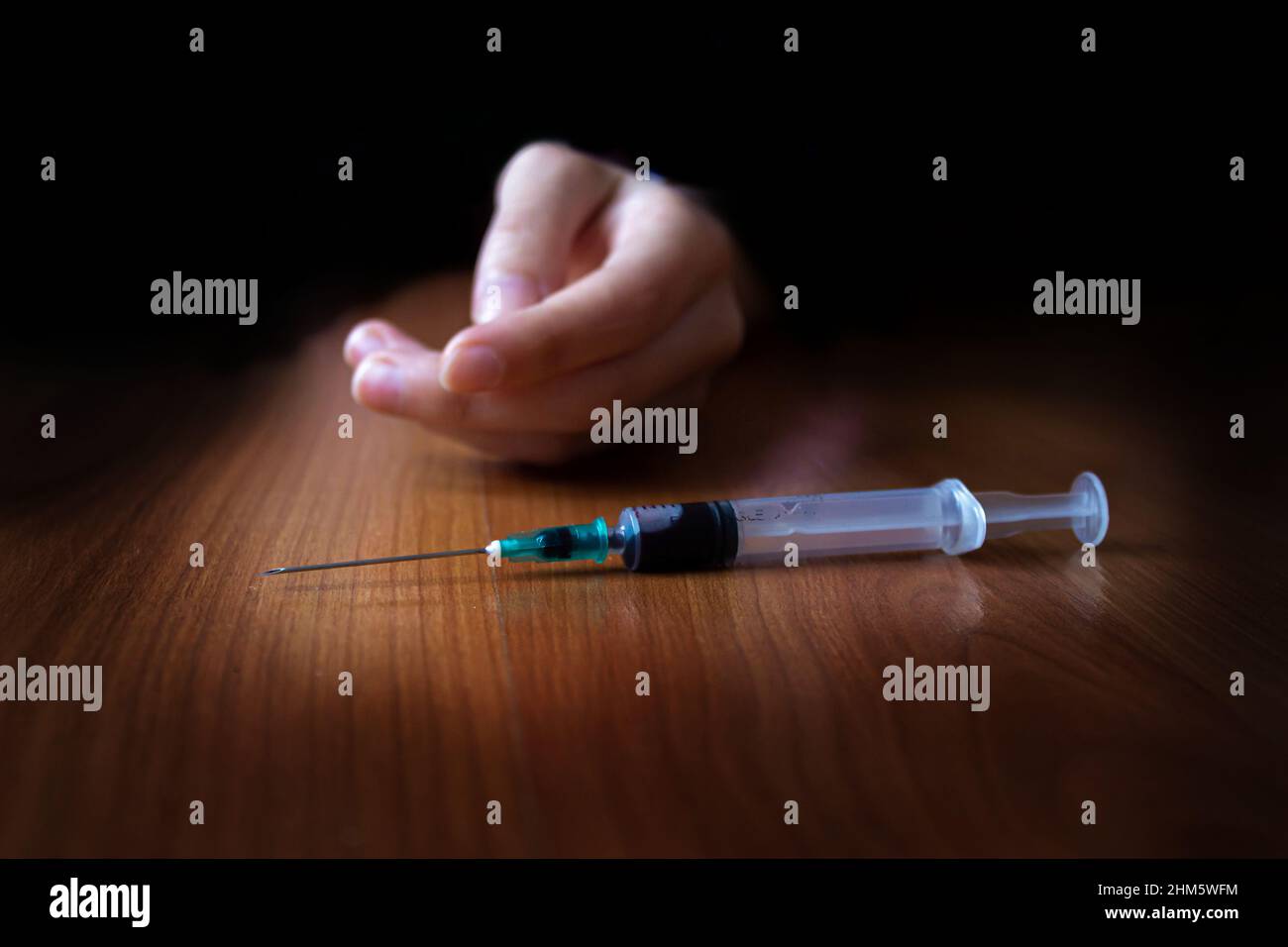 Drug addiction concept. Young woman slumped on the floor trying to reach for a drug syringe. Stock Photo