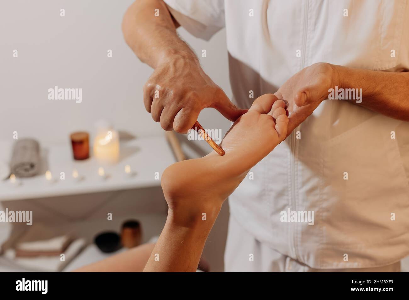 Reflexology foot massage with wooden thai stick. Acupressure in alternative medicine. Oriental physiotherapy through energy points on body. Bodycare and SPA in Thailand. Stock Photo