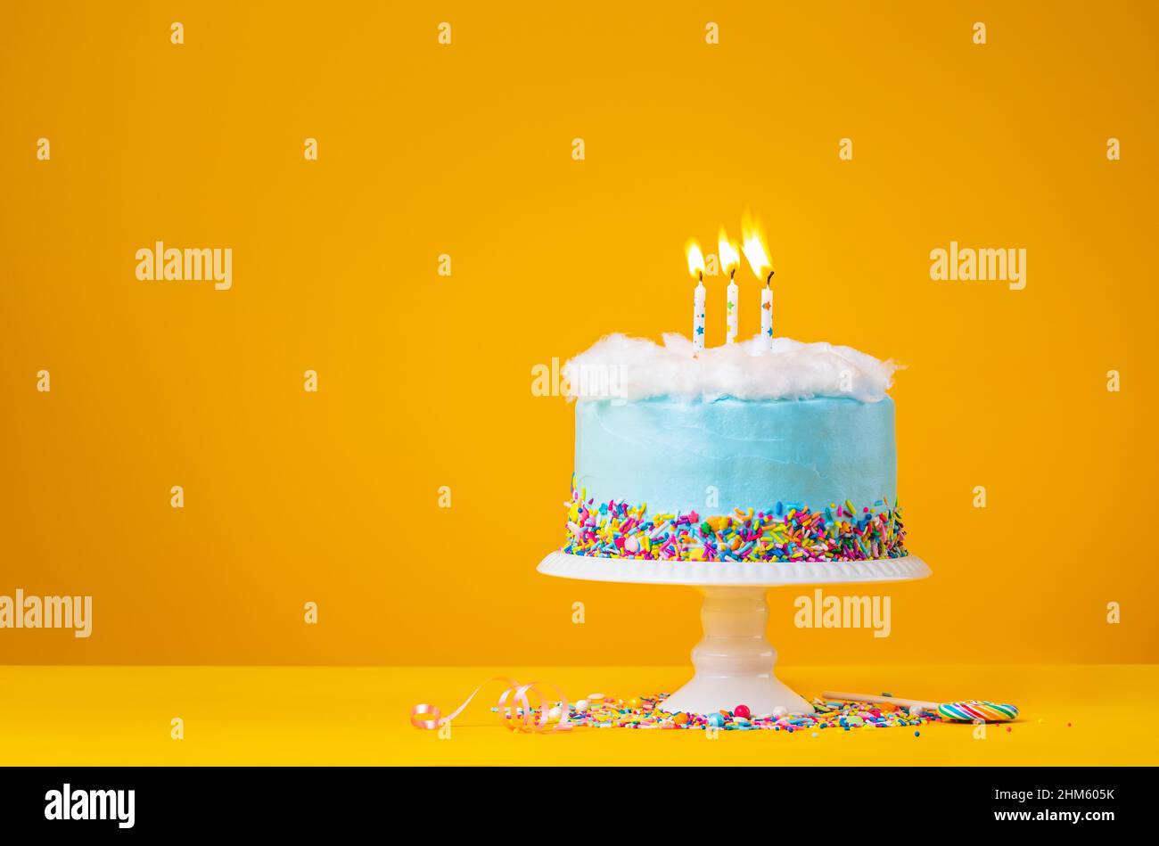 Blue Birthday Cake with three Candles over a yellow Background Stock Photo