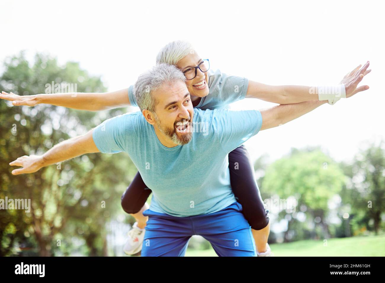 outdoor senior fitness woman man lifestyle active sport exercise healthy fit retirement love fun piggyback Stock Photo