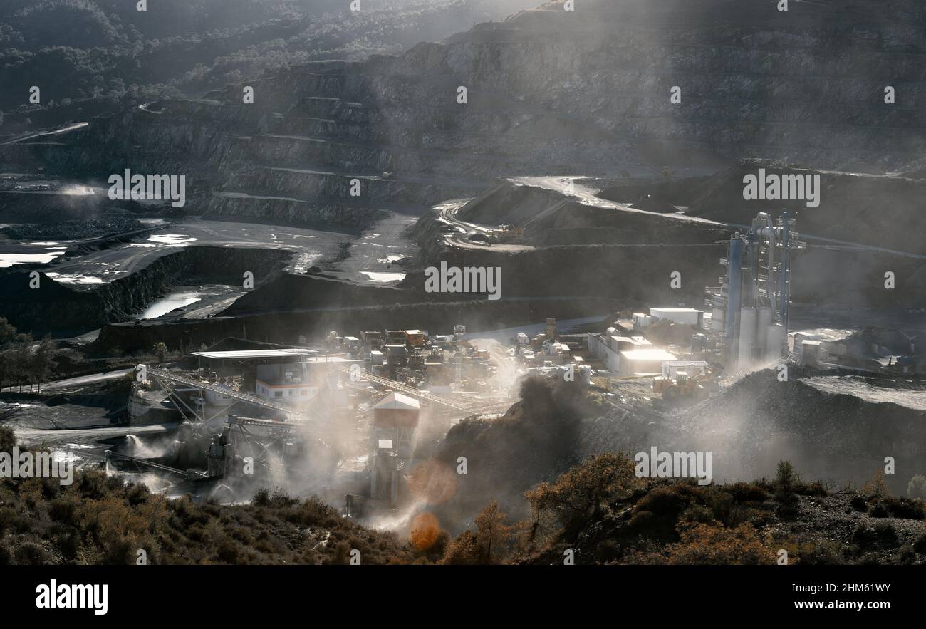 Mining plant in stone quarry in clouds of dust from production, backlit dramatic landscape with sun flare Stock Photo