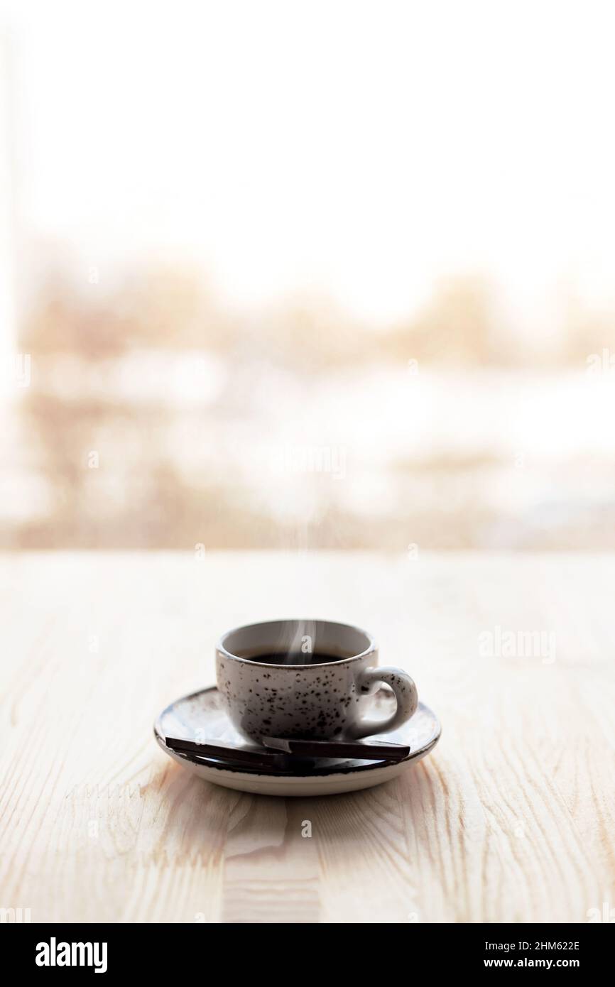 Cup of coffee espresso on saucer on wooden table near window blurred city background. Stock Photo