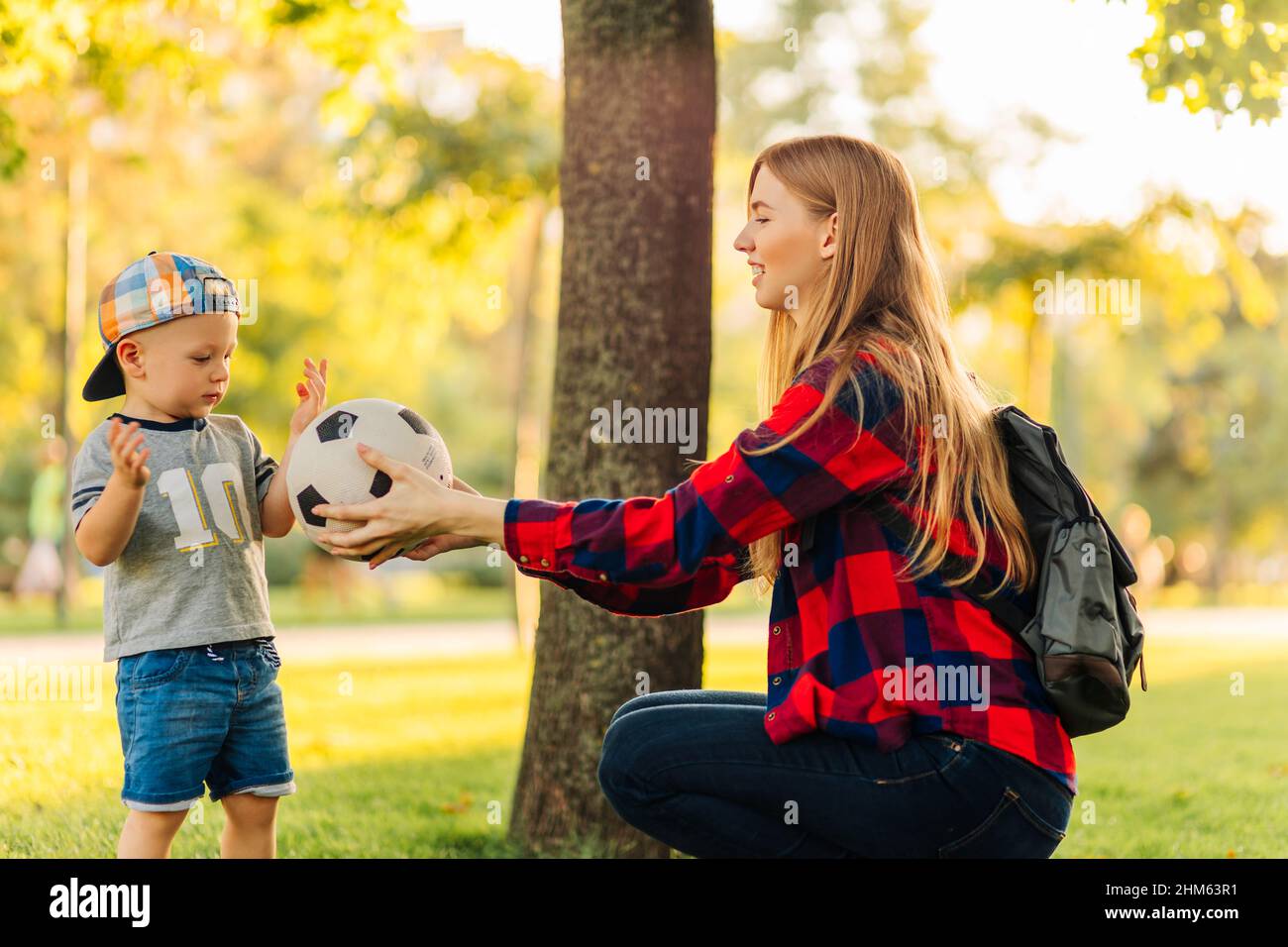 Young happy mom with little son play football in the park, mom gives ...