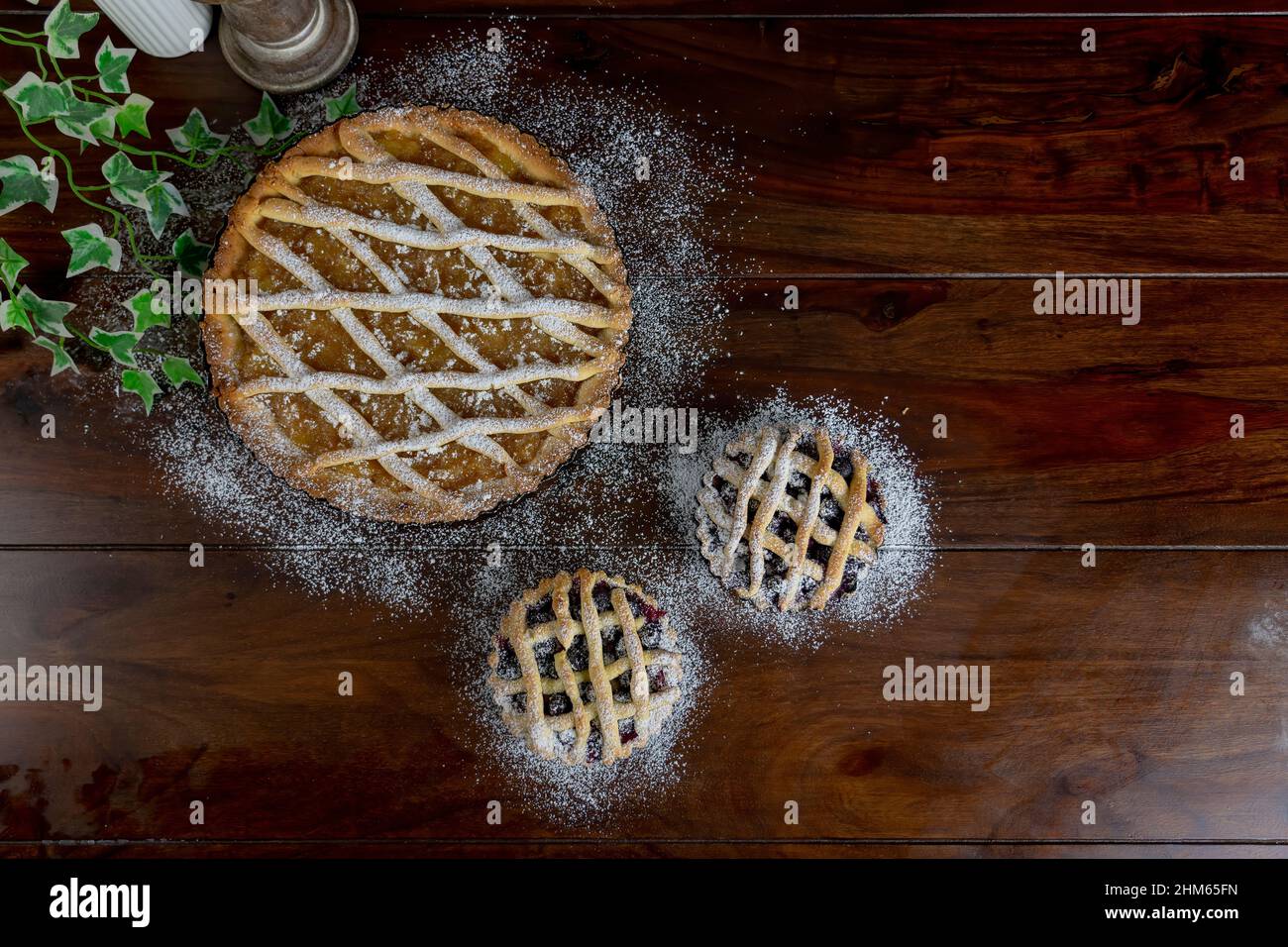 Top view Delicious apple pie large and two small blue berry tarts on wood table background. Stock Photo