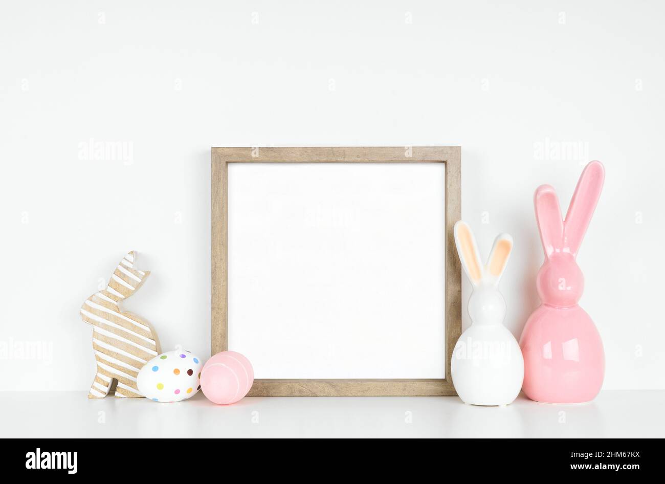 Mock up wood frame with Easter egg and bunny decor on a white shelf. Square frame against a white wall. Copy space. Stock Photo