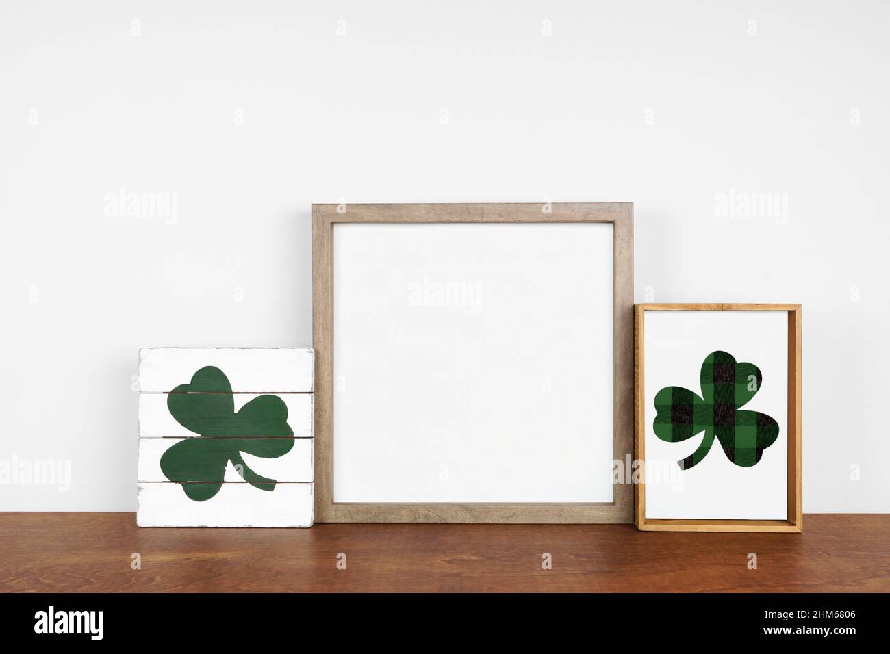 Mock up wood frame with St Patricks Day decor on a wood shelf. Rustic wood signs. Square frame against a white wall. Copy space. Stock Photo