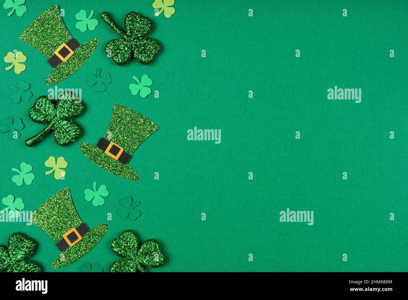 St Patricks Day shamrock and leprechaun hat side border. Top down view over a green paper  background with copy space. Stock Photo
