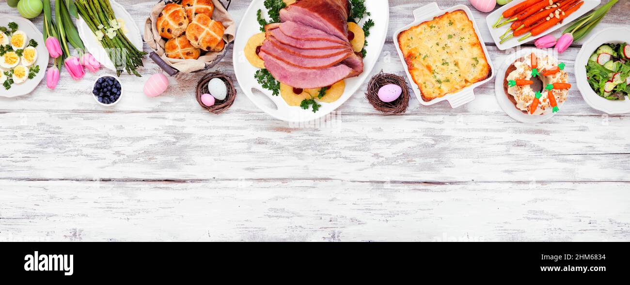 Traditional Easter ham dinner. Overhead view top border on a white wood banner background with copy space. Ham, scalloped potatoes, vegetables, eggs, Stock Photo