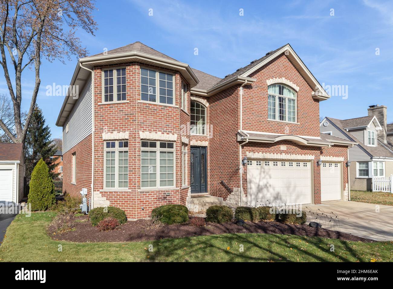 A large, two story red brick home with a three car garage. Stock Photo