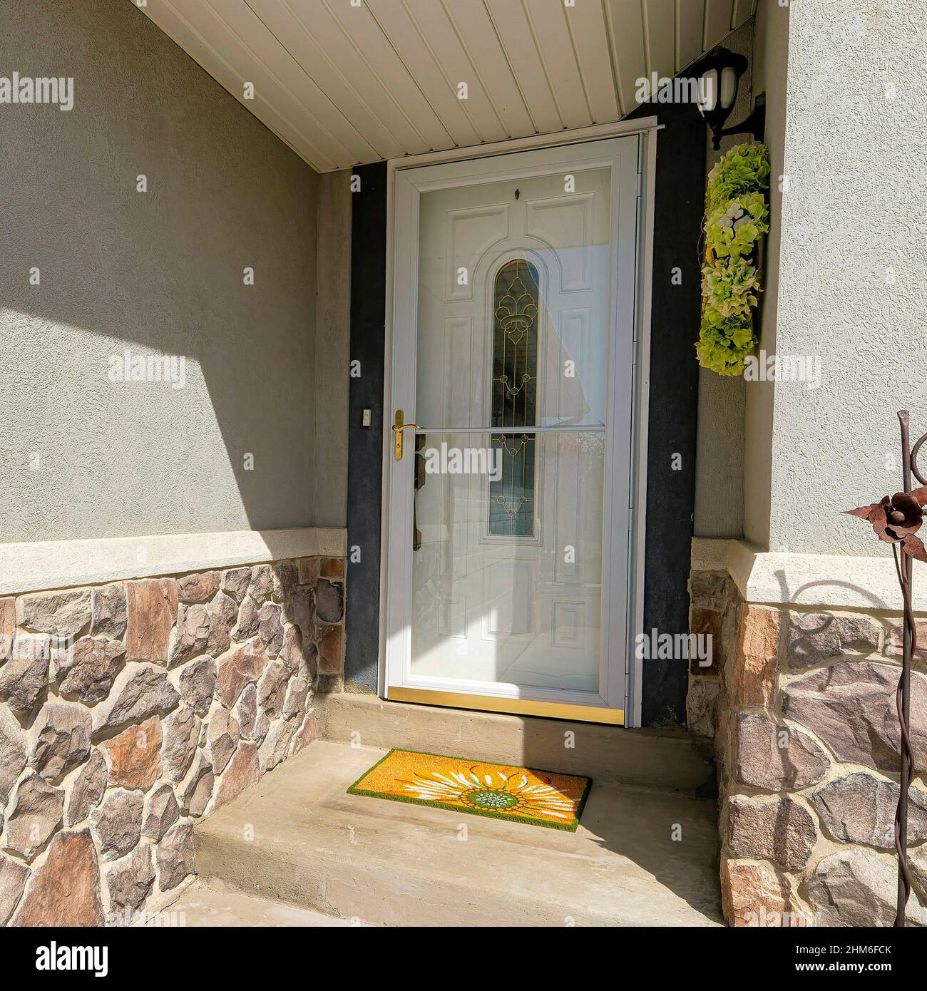 Square Home entrance beside the garage with glass storm door and white door with ornate glass Stock Photo